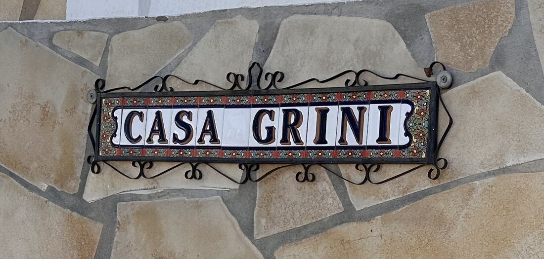 Håndmalt keramikkskilt med navnet Casa Grini på steinmuren ved inngangen